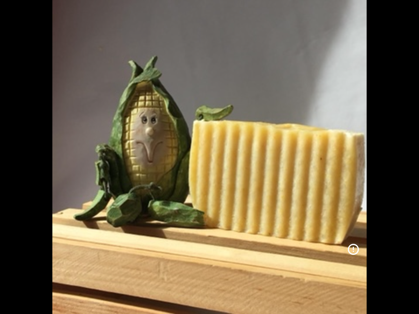 Corn soap with a corn guy sitting next to it,  on top of a wooden box.